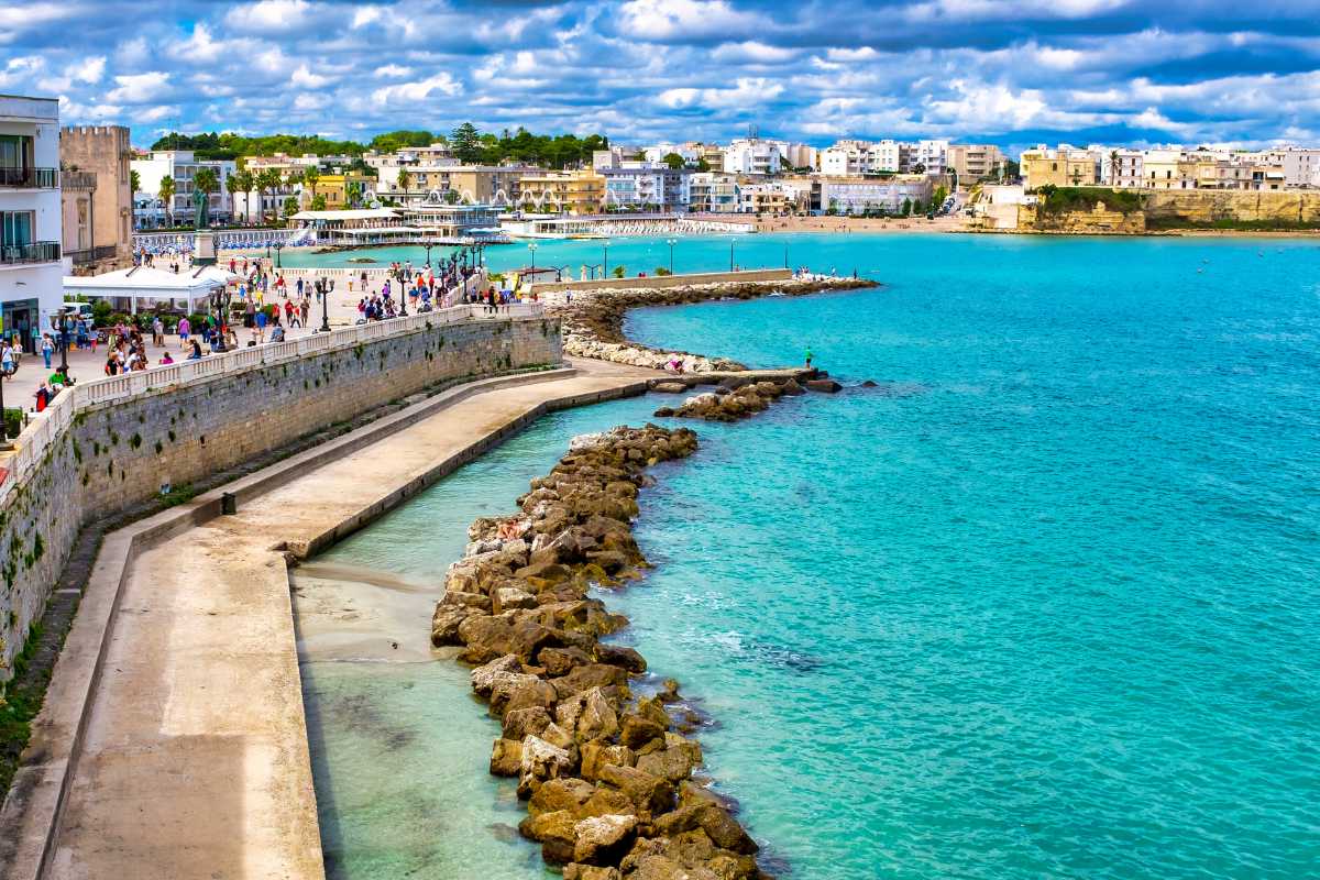 Sentiero costiero tra Otranto e Torre Sant’Emiliano, con mare blu intenso, scogliere e vegetazione mediterranea, atmosfera estiva e avventurosa.