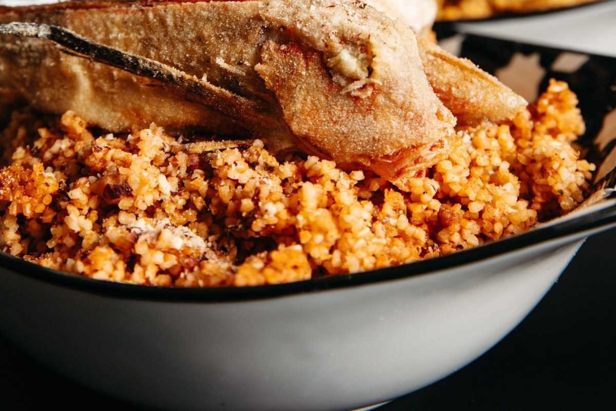 Scorcio di una tavola imbandita con piatti tipici di pesce, all’aperto, vista sulla città vecchia di Otranto e il mare sullo sfondo